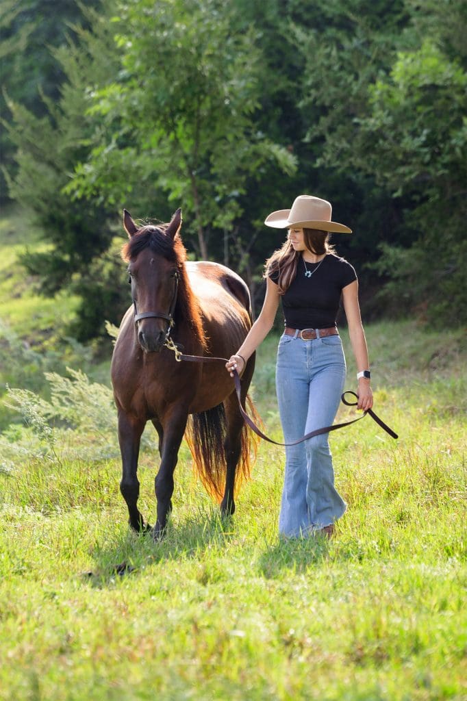 young woman in western hat walking her horse
