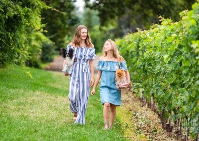 two young women walking in the vineyard with dogs in bags over their shoulders